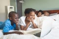 Happy African American children using laptop while parents relaxing on bed in bedroom Royalty Free Stock Photo