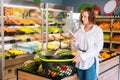 Front view of happy attractive young woman browsing shopping list using mobile phone standing with basket. Royalty Free Stock Photo