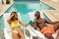 Couple toasting glasses of cocktail while relaxing on a sun lounger near swimming pool Royalty Free Stock Photo