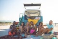 Group of friends looking at camera while sitting near camper van at beach Royalty Free Stock Photo
