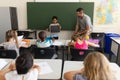 Front view of happy schoolboy holding slate board and standing at greenboard in classroom Royalty Free Stock Photo