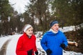 A front view of senior couple jogging in snowy winter nature.