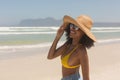 Young African American woman in yellow bikini, hat and sunglasses standing on the beach Royalty Free Stock Photo