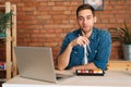 Front view of happy young Caucasian man eating sushi rolls with chopsticks sitting at working desk with laptop at home Royalty Free Stock Photo