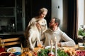 Front view of happy young couple in love sitting at festive Christmas table with Akita dog during holiday family party.