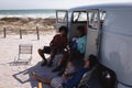 Happy young men relaxing near camper van at beach in the sunshine Royalty Free Stock Photo