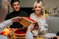 Front view of happy young woman receiving gift from loving mother-in-law sitting with family at dinner feast table at Royalty Free Stock Photo