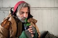 A front view of homeless beggar man sitting outdoors, holding bottle of alcohol. Copy space. Royalty Free Stock Photo