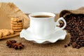 Front view of hot black coffee in white elegant cup with saucer, sweet cookies and scattering of coffee beans on rural sackcloth Royalty Free Stock Photo