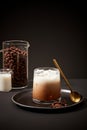 Front view of an iced milk coffee placed on a tray with a metal spoon. Coffee beans and fresh milk in beaker. Minimalist black
