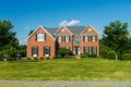 Front view of a large brick country house. Large freshly cut lawn and trees in the foreground