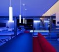 Front view living room with table and a red sofa lit by blue LEDs and lamps attached to the ceiling. Large window overlooking the