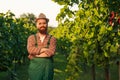 Front view looking at camera young winemaker man farmer hat crossed arms vineyard smiles cheerfully.