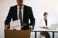 Front view with the male employee standing holding office supplies in the paper box going to submit a resignation letter while a