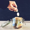 Front view of man hand putting coins into a glass jar with paper Royalty Free Stock Photo