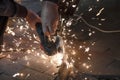 Front view of a man`s hands working on a metal part of a garden bench, using an electric grinder while sparks are flying around i Royalty Free Stock Photo