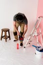 front view of man in working overall and headband dipping paint roller into roller tray