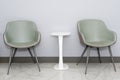 Front view of modern simple chairs with white table against grey wall in a minimal style waiting room interior. Chairs in