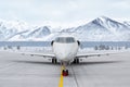 Front view of the modern white corporate airplane at the airport apron on the background of high scenic snow capped mountains