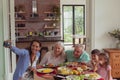 Multi-generation family taking selfie with mobile phone while having food on dining table Royalty Free Stock Photo