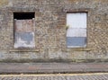 Front view of an old abandoned derelict house on an empty street with boarded up windows and dilapidated brick walls