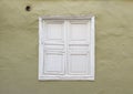 Front view of old closed white wooden square window on green rough facade and ventilation hole. Grunge and vintage construction