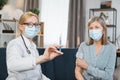 Front view of pleasant likable blond woman doctor, in face mask, holding a syringe with vaccine or medicine, ready to Royalty Free Stock Photo