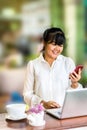 Front view portrait of Asian businesswoman sitting at long table in coffee shop and using laptop computer and chatting on cell pho Royalty Free Stock Photo