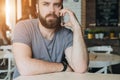 Front view. Portrait of attractive young bearded hipster man sitting in cafe at table and talking on his cell phone. Royalty Free Stock Photo