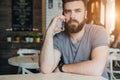 Front view. Portrait of attractive young bearded hipster man sitting in cafe at table and talking on his cell phone. Royalty Free Stock Photo