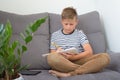 Front view portrait of diligent schoolboy writing or drawing, sitting on grey sofa while doing homework. Studying online