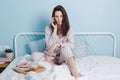 Portrait of thoughtful serious confident brunette friendly smart girl sitting on bed talking on phone, drinking coffe Royalty Free Stock Photo