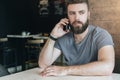 Front view. Portrait of young handsome bearded hipster man sitting in cafe at table and talking on his cell phone. Royalty Free Stock Photo