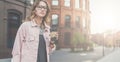 Front view. Portrait of young woman in glasses standing outdoors and holding a cup of coffee. Royalty Free Stock Photo