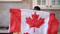 Front view positive African American man shacking Canadian flag posing in kitchen indoors. Portrait of happy confident