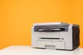 Front view of a printer and a stack of A4 paper on a white table against a yellow background Royalty Free Stock Photo