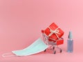 Red gift box on shopping cart with medical face mask and alcohol hand spray on pink background with copy space. Covid19