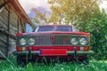 Front view of a red vintage Lada car in the countryside. Old wooden barn from the side. Old red Soviet car Royalty Free Stock Photo
