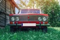 Front view of a red vintage Lada car in the countryside. Old wooden barn from the side. Old red Soviet car Royalty Free Stock Photo