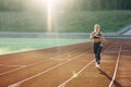 Front view of running caucasian woman in black sportswear doing cardio workout on sports track of stadium. Adult female