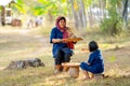 Front view of senior Asian woman with traditional clothes winnow rice using basketry and little girl stay beside and also work