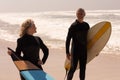 Senior couple with surfboard standing on beach and looking each other