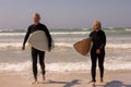 Senior couple with surfboard walking on beach
