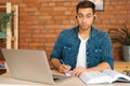 Front view of serious male student studying online from home using laptop, writing notes, watching video class lesson Royalty Free Stock Photo