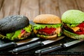 Front view of set of three color homemade burgers with marble beef with knifes wooden table Royalty Free Stock Photo