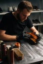 Front view of shoemaker wearing black latex gloves applying paint on light brown leather shoes and rubbing with fingers.