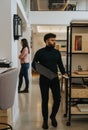 A front view shot of male employee changing working area, carrying lap top and walking at the office.