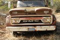 Old, rusted GMC truck sits abandoned by the side of a back rural road.