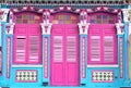 Exterior of blue Singapore Straits Chinese Peranakan shophouse with arched windows, pink wooden louvered shutters & ornate columns