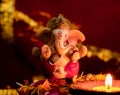 Front view of small ganesha statue and clay lamp against blurred red golden chunari in the background. hinduism concept Royalty Free Stock Photo
